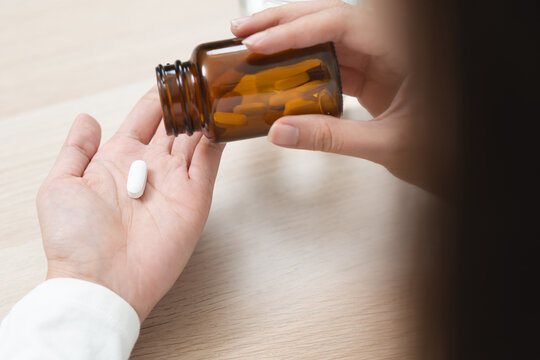 Close up of a person pouring a white pill from a brown medicine bottle into hand