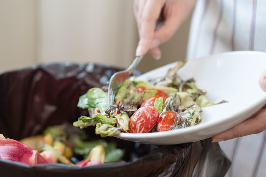 The housewife is throwing the leftover food from the meal into the bin