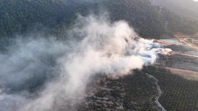 Aerial drone view of landfill fire spreading smoke over forest