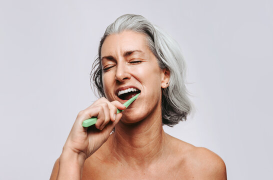 Mature woman brushing teeth with toothbrush in studio