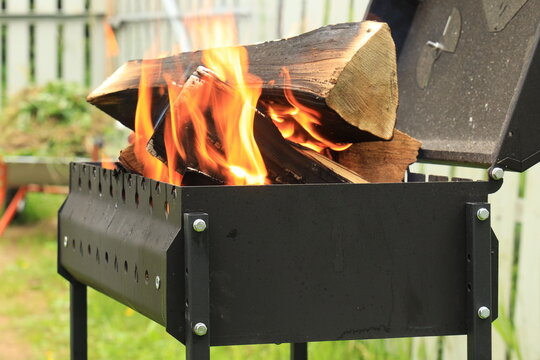Large firewood burns with a beautiful orange flame and is charred in an open black brazier