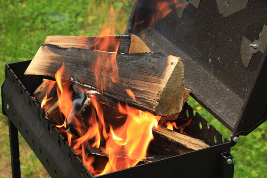 Black brazier with open lid and burning logs and green background