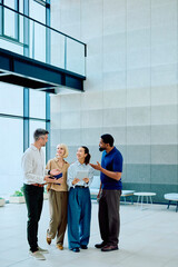 Group of diverse business people conversing and collaborating while standing in a modern office lobby, discussing new ideas © we.bond.creations