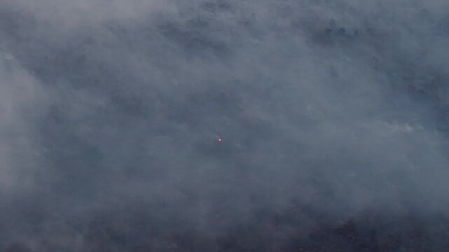 Smoke drifts slowly across a dark, foggy sky