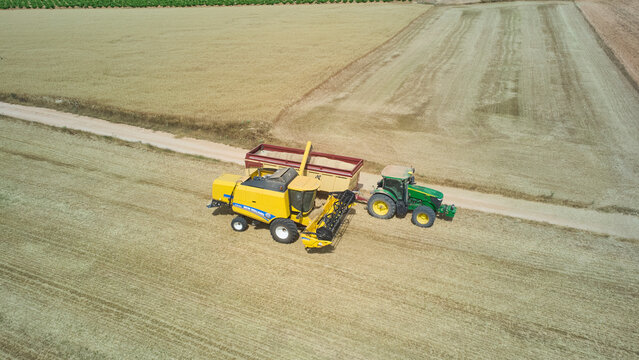 Aerial view of combine unloading harvested wheat grain into tractor trailer in field. Castilla-La Mancha, Spain - June 7, 2026.