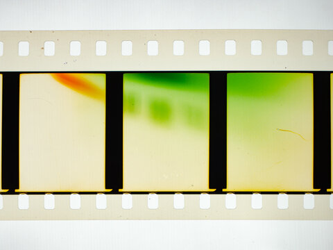 Vintage 35mm motion picture film strip featuring blank frames and classic sprocket holes. Authentic analog cinema celluloid isolated on white with green and orange light leak color effects