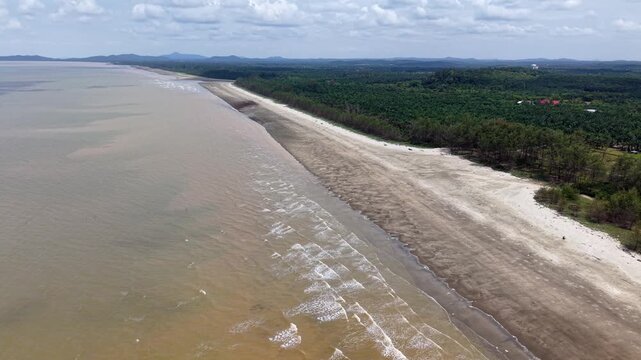 Wide beach meets murky water under cloudy skies