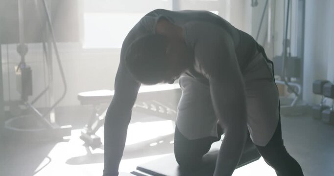African American man picking up dumbbell beside bench at home gym, rowing to build back strength