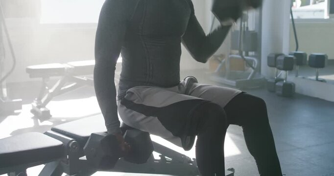 African man in compression top reaching for right dumbbell and curling it on bench for strength