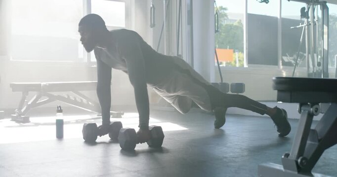 African-American man holding plank starting rows rotating to pushup with dumbbells for core at gym