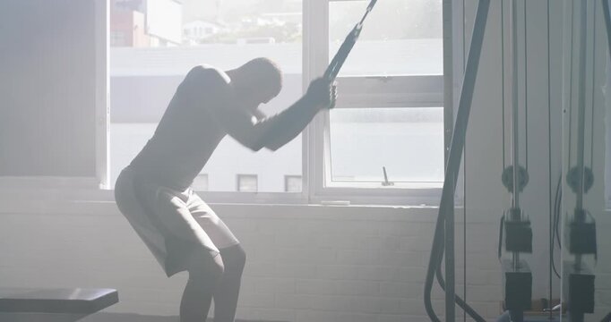African man in athletic wear gripping rope performing triceps pulls training at gym checking watch