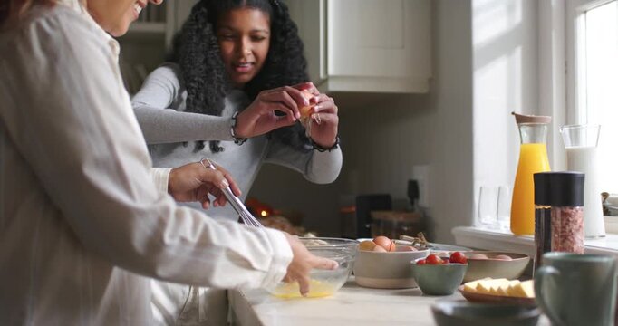 African American mother guiding child cracking eggs pouring into glass bowl whisking for breakfast