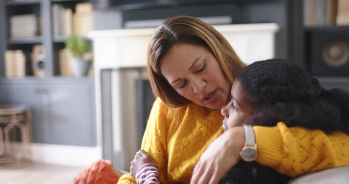 African American mother pulling child close, cradling and comforting on couch with orange throw
