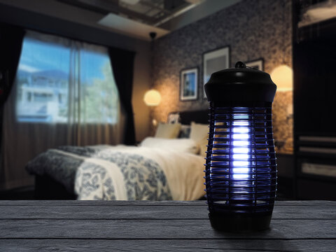 insects mosquito electric blue light killer lamp is put on nice wooden table in nice bedroom with background of bed and windows to protect repellent mosquito and other insects 