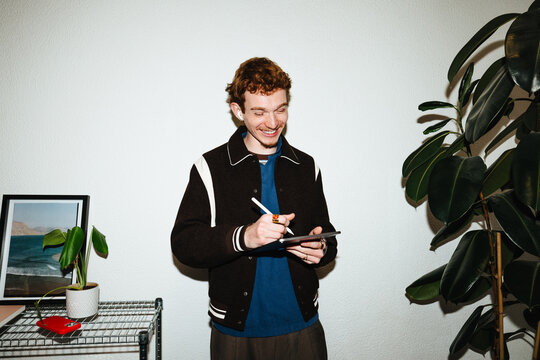 Young man using tablet and smartphone with stylus for creative work indoors
