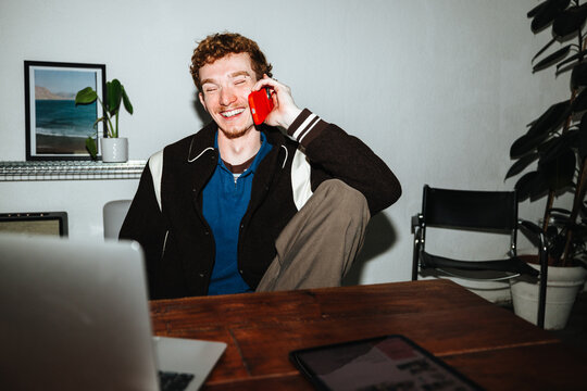 A man balances work and a phone call at his desk with a laptop nearby.