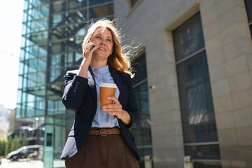 Fototapeta premium Businesswoman talking on phone with coffee in city