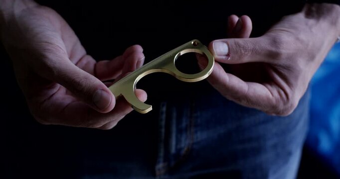 Close up of hands holding and turning a brass touchless hygiene hook tool in daylight