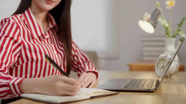 Woman working with a notebook and laptop at a desk, ideal for note taking, planning, productivity, study, office work, home office and professional lifestyle concepts.