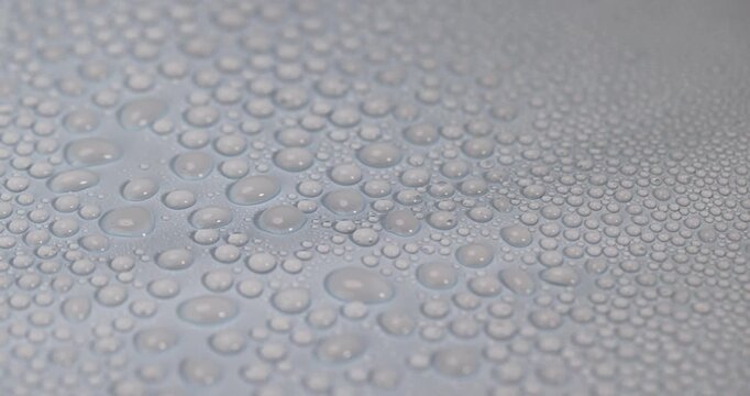Water condenses on plastic, pure water in the form of small and large droplets on a smooth blue material under studio lighting with an authentic look and a clear contour.