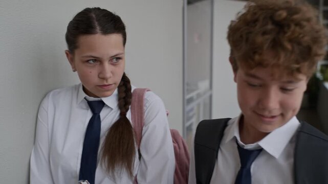 Portrait of Caucasian teenage girl leaning against school wall looking sad while classmate walks past. Footage representing school bullying, social exclusion, or teenage mental health concepts