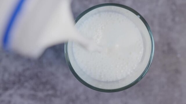 Top view close-up video of fresh white milk being poured into a clear glass, surrounded The creamy white milk fills the glass