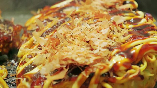 Japanese okonomiyaki on a hot griddle with sauce, mayonnaise and bonito flakes