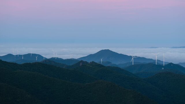Timelapse of a Wind Turbine Farm on a Forested Mountain Ridge at Sunrise. Wind turbines generate clean renewable energy.	