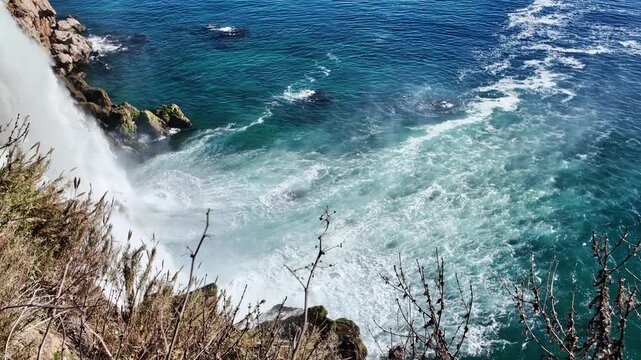High angle view of lower duden waterfall cascading into turquoise and blue sea with white foam and rocky shore antalya.