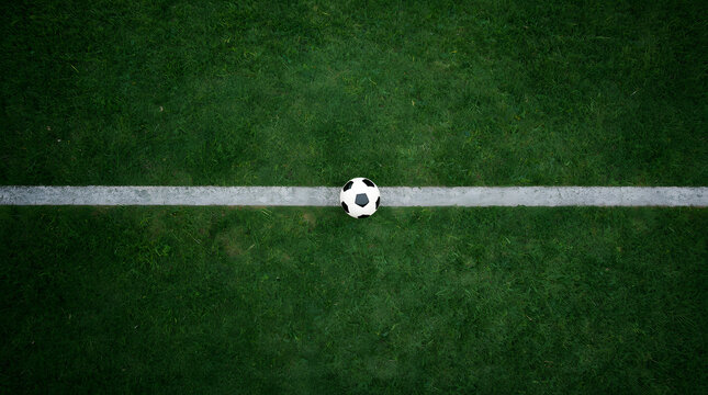 Soccer Ball on Field Line: A soccer ball rests centered on the white line marking a green football pitch, symbolizing the start or continuation of a game.