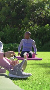 Vertical video: Settling group, woman in gym warming up on mat on grass doing butterfly with bottle