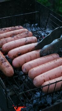 Vertical video. Grilling sausages during summer picnic. Summer weekend activity, barbecue. 