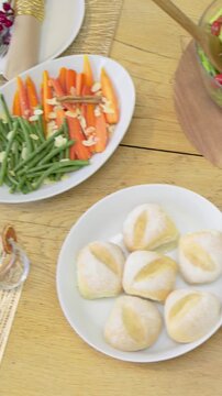 Vertical video: Drifting camera revealing home table meal spread with salad showcasing bread rolls