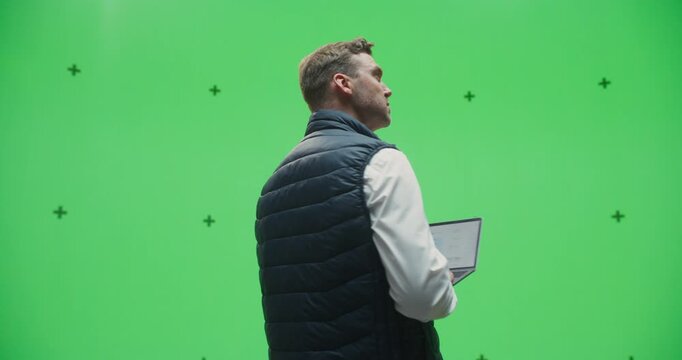 360 Degree Green Screen Chroma Key. Man Holding Laptop and Typing, Working on Computer, Analyzing Data and Browsing Information. Orbital Cinematic Arc Tracking Shot.