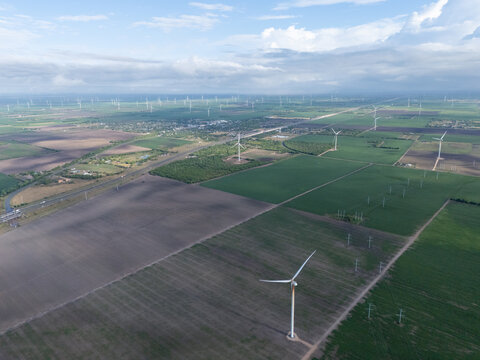 Wind turbines stand tall in neat rows against a vast agricultural landscape, rotating to generate clean, renewable electricity near harlingen, texas, along road 402