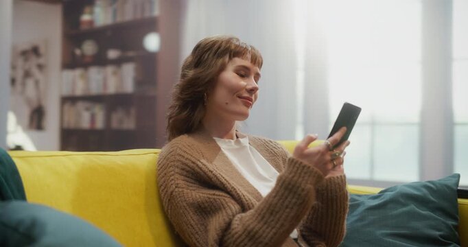 360 Degree. Caucasian Woman Relaxes on a Home Couch Using a Smartphone to Shop Online, Scroll Social Media Apps, Send Messages, Make Internet Purchases, and Complete Remote Work Tasks. Tracking Shot.