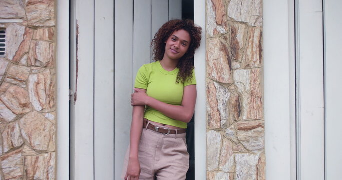 Smiling teenage girl leaning against doorway, relaxed and confident, natural charm and happiness, standing in casual pose with arms crossed, exuding warmth and positivity