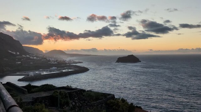 Beautiful golden sunset over the coastal town, modern harbor marina, and volcanic islet Roque de Garachico in Tenerife, Canary Islands, with dramatic evening clouds over the Atlantic Ocean.