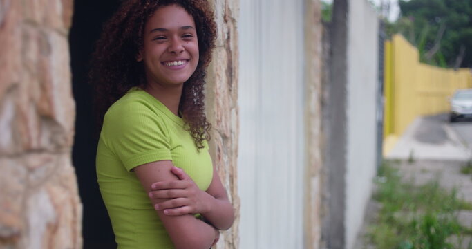 Smiling teenage girl leaning against wall, relaxed and confident, exuding natural charm and happiness, standing with arms crossed, radiating positivity and warmth