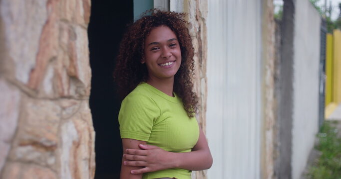 Smiling teenage girl leaning against wall, relaxed and confident, exuding natural charm and happiness, standing with arms crossed, radiating positivity and warmth
