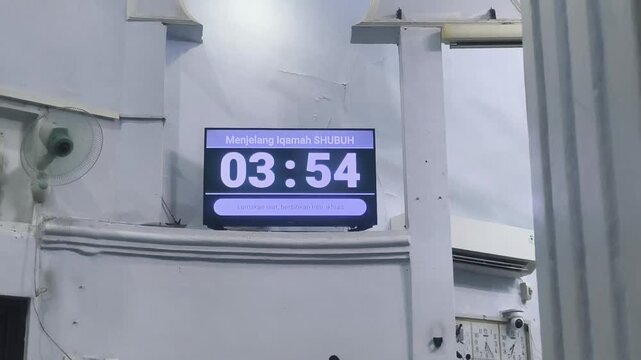 A digital countdown timer displayed on a television screen inside a mosque, showing the remaining time before the Fajr (Shubuh) prayer begins.
