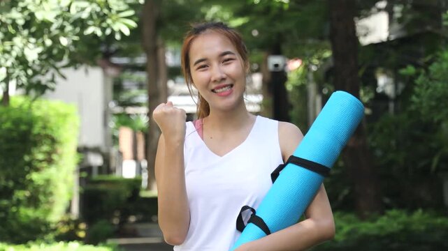 Happy and healthy asian woman carrying yoga mat to yoga class