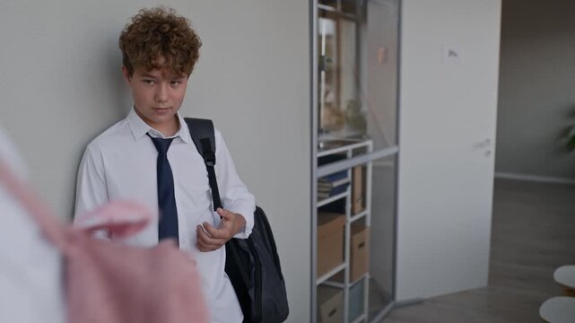 Caucasian teenage girl knocking book out of Caucasian teenage boys hands in school hallway. Perfect for campaigns addressing school bullying, teenage mental health, and student conflict
