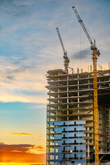 High-rise building under construction with cranes against colorful evening sky © Levon