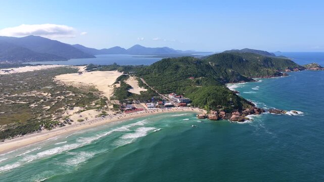 Wide aerial view of Joaquina Beach, sand dunes, ocean waves, and hills in Florian&oacute;polis.