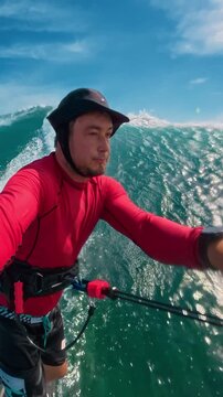  A male kitesurfer in a red sweater and sunhat films himself riding a huge ocean wave. Extreme sports