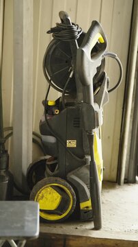 A yellow and black Karcher high-pressure washer with a spray gun and hose reel standing in a garage.