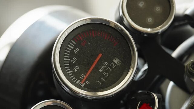Close-up of a classic round motorcycle speedometer showing speed scale and mechanical odometer
