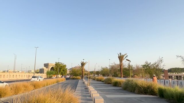 Scenic walk by a Wadi Al Aqeeq sign overlooking a rocky riverbed and bridge at sunset.