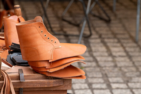 Stack of unstitched light brown leather shoe uppers sitting on a wooden bench at an artisan market